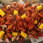 A top-down view of a traditional spicy crawfish boil, featuring bright red crawfish, corn, and potatoes, illustrating how to eat crawfish.