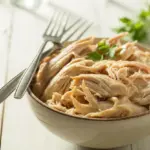 A close-up of a bowl of juicy shredded chicken, freshly prepared and ready for various recipes like tacos or salads.