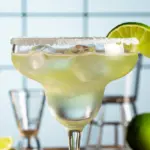 A classic margarita on the rocks in a salted rim glass, garnished with a lime wedge, showing how to make a classic margarita.
